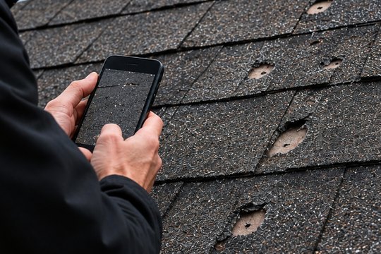 Roofer photographing hail damage on shingles with a phone